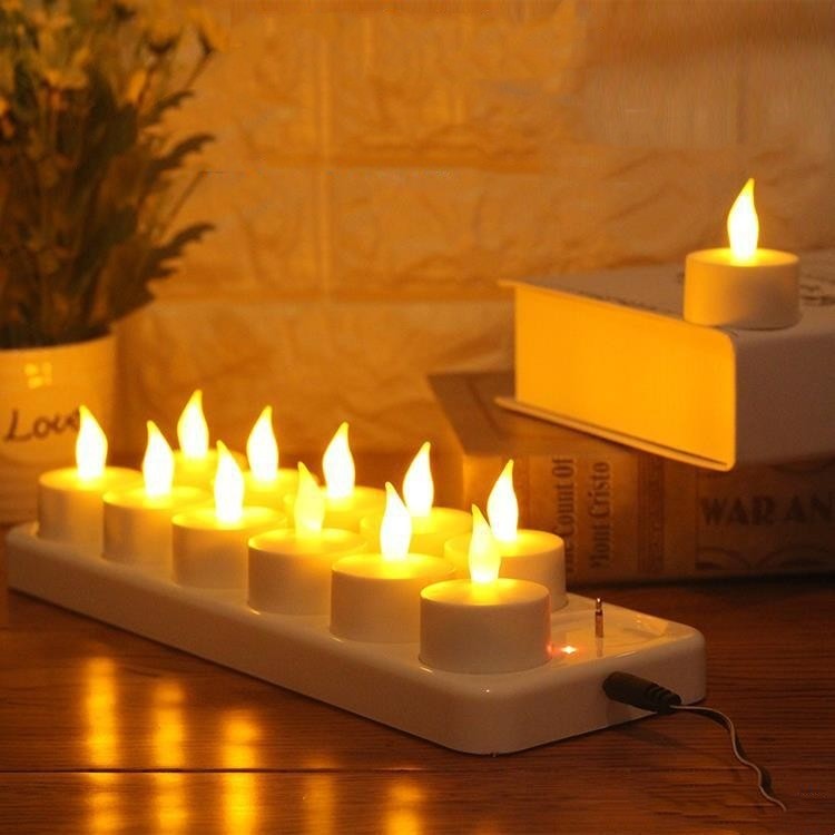 Douze bougies chauffe-plat LED allumées sur leur socle de recharge, lumière ambrée