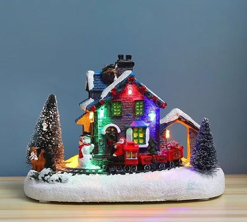 Chalet de Noël enneigé en résine illuminé de lumières multicolores, avec sapins et bonhomme de neige