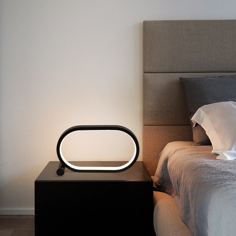 Lampe anneau ovale noire allumée sur une table de chevet