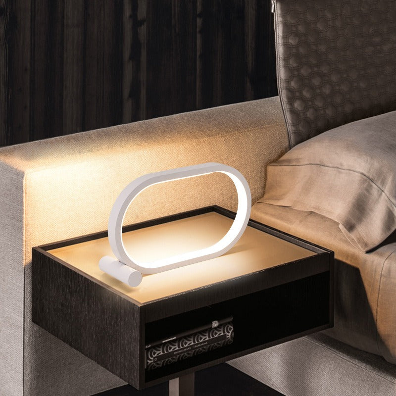 Lampe anneau ovale blanche posée à l’horizontale sur un chevet
