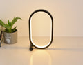 Lampe anneau ovale noire, lumière chaude, à côté d’une plante