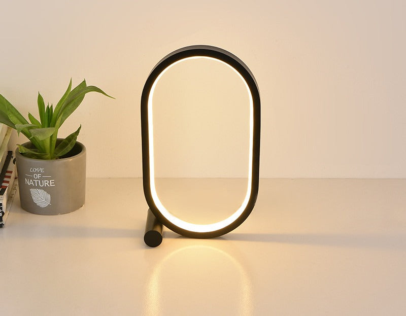 Lampe anneau ovale noire, lumière chaude, à côté d’une plante