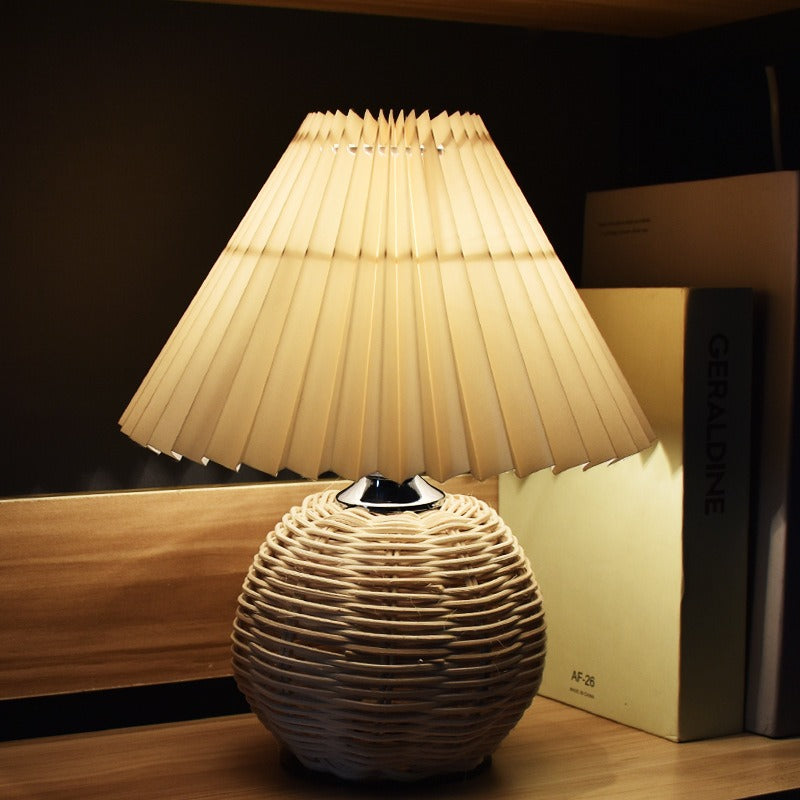 Lampe à abat-jour plissé allumée, socle tressé, dans une chambre