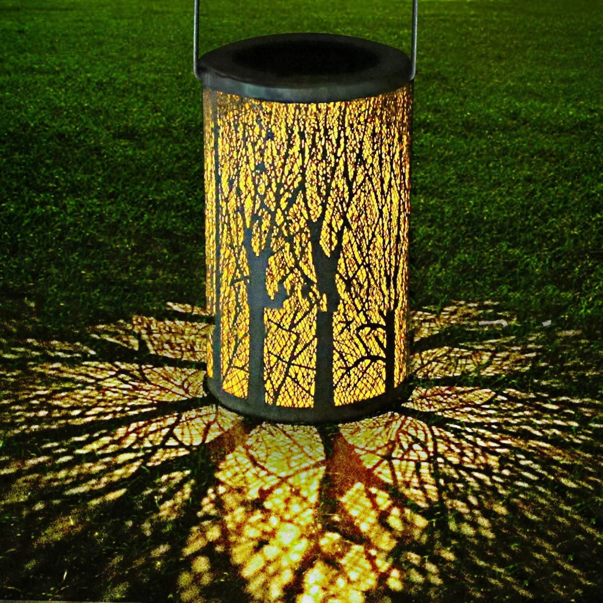 Lanterne solaire à motif d’arbre projetant des ombres au sol, la nuit