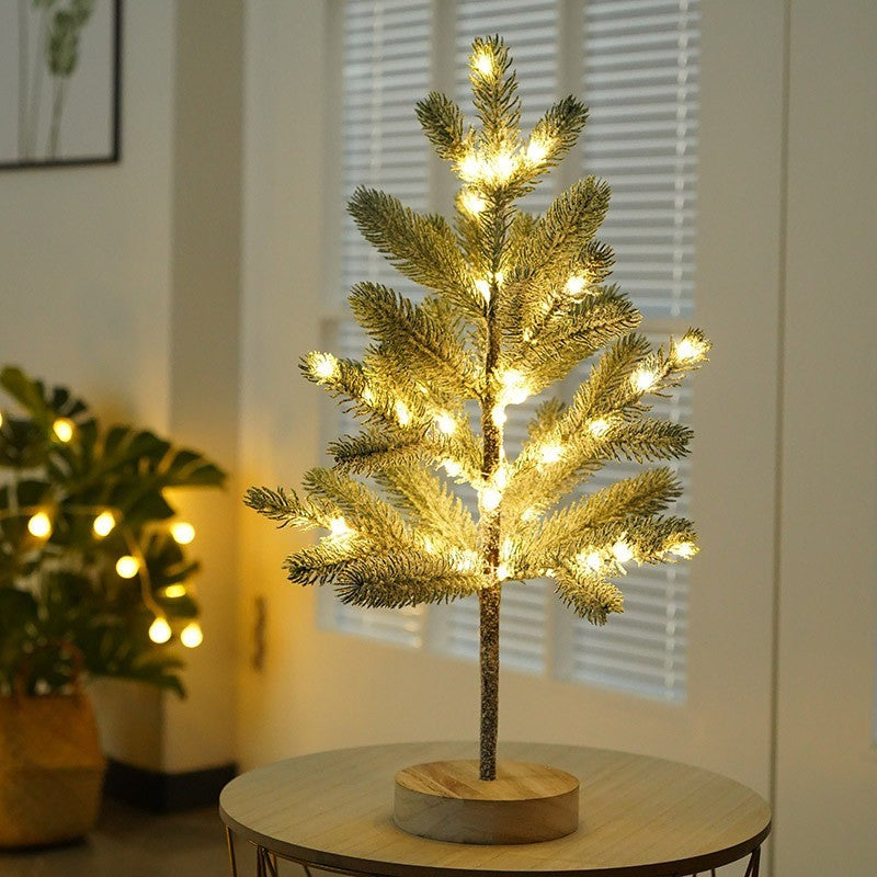 Petit pin enneigé lumineux sur socle en bois, devant une fenêtre