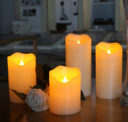Trois bougies LED en cire posées sur une table, flamme ambrée