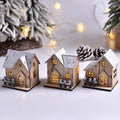 Trois maisonnettes en bois au toit enneigé éclairées, devant un sapin