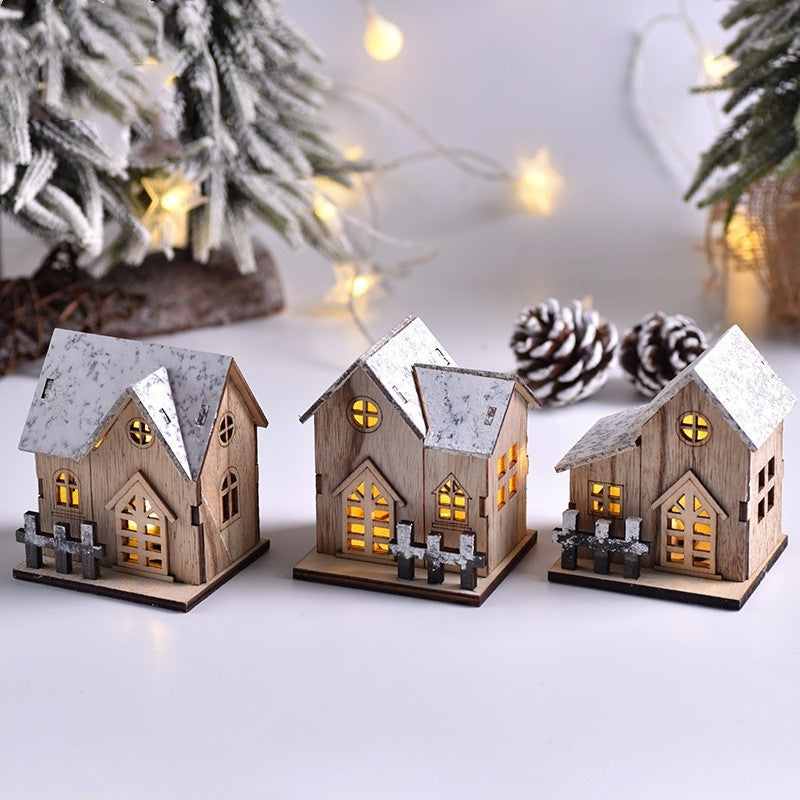 Trois maisonnettes en bois au toit enneigé éclairées, devant un sapin