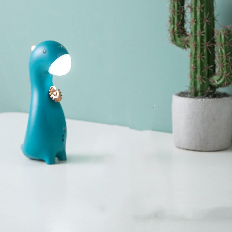 Veilleuse petit dinosaure bleu canard allumée sur un bureau