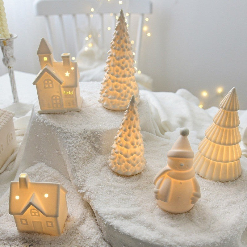 Village de Noël en céramique blanche éclairé : maisons, sapins et bonhomme de neige sur un lit de neige